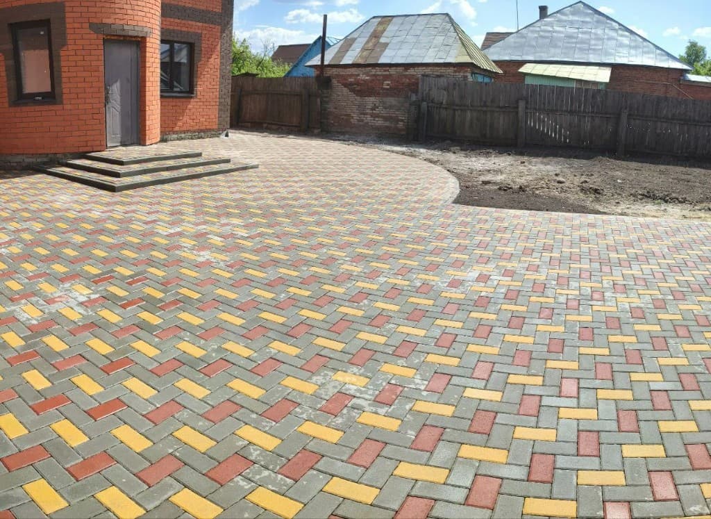 Широкое мощение двора брусчаткой ёлочкой у кирпичного дома